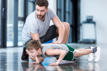 Boy doing push ups with coach at fitness center