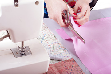 Fashion designer concept. Womans hands cutting pink fabric in studio. Pattern background