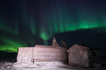 wooden house, yurt hut on the background the polar Northern aurora borealis lights in Norway Svalbard in the mountains