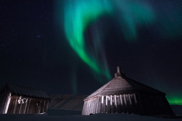 wooden house, yurt hut on the background the polar Northern aurora borealis lights in Norway Svalbard in the mountains