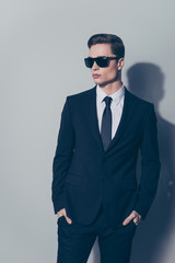 Young attractive businessman in sunglasses put his arms into pockets. He is wearing formal wear