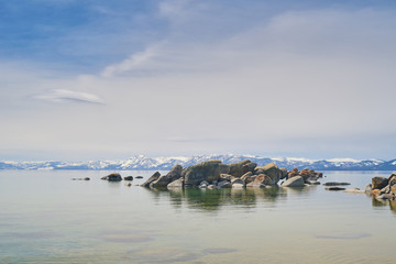 Boulders in water of the lake Tahoe, mountains covered by snow at background