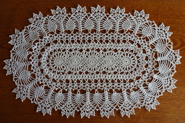 Oval white crochet lace handmade doily on wood from above