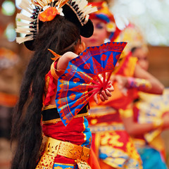 Asian travel background. Group of beautiful Balinese dancer women in traditional Sarong costumes with fans in hands dancing Legong dance. Arts, culture of Indonesian people, Bali island festivals. © Tropical studio