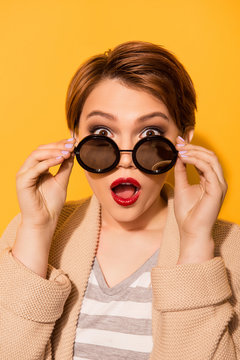 Omg! Close up portrait of amazed girl with red pomade in stylish sunglasses and casual wear on the bright yellow background