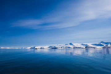 landscape of the Arctic Ocean and reflection with blue sky and mountains with snow on a sunny day, Norway, Spitsbergen, Longyearbyen, Svalbard, summer, winter