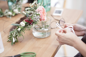 blurred background of female hands weaving white ribbon againts flower crown