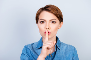 Shh! Girl is showing someone to keep quiet and to tell her secret on light blue background