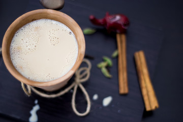 Indian tea chai masala karak with spices and milk, in a clay glass on a wooden background. Above, selective focus
