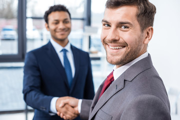 Handsome young businessmen shaking hands and smiling at camera, business concept