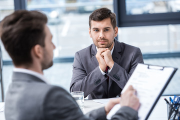 Handsome young businessman looking at manager with clipboard at job interview, business concept