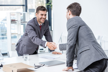 Two smiling businessmen shaking hands at meeting in office, business concept