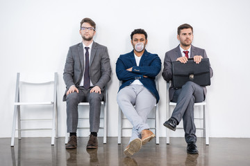 young businessmen sitting on chairs in waiting room, business concept