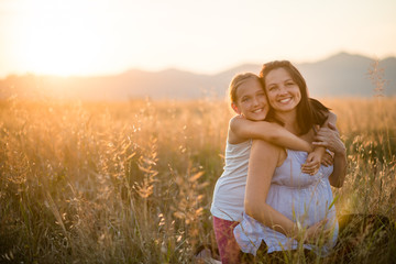 Pretty daughter hugging her pregnant mother from behind