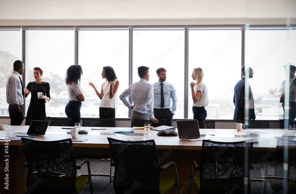 Poster businesspeople stand and chat before meeting in boardroom