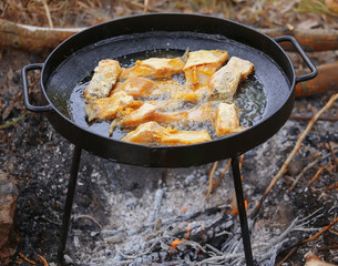 Boiling in oil on opened fire, frying fish fillet.