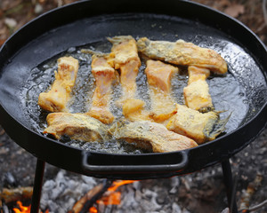 Boiling in oil on opened fire, frying fish fillet.