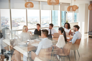 Businesswoman Leads Meeting Around Table Shot Through Door