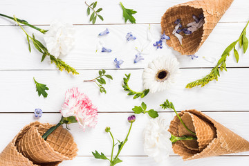 Top view of beautiful blossom flowers and green leaves in waffle cones on wooden table