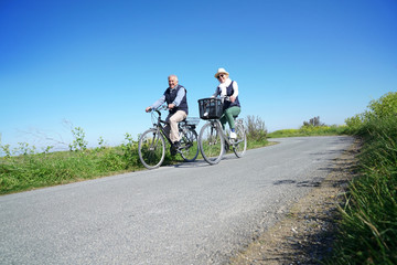 Fototapeta na wymiar Senior couple riding bike together on country road
