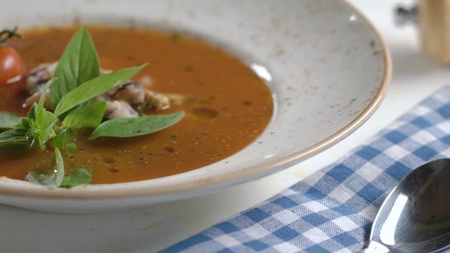 Tomato soup with seafood decorated with basil leaves and cherry tomatoes in white plate on the table.