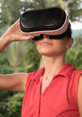 Closeup portrait of woman having fun with virtual reality glasses over green tree background