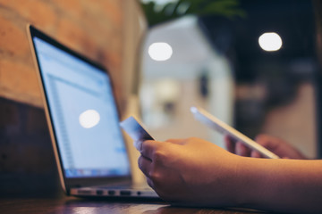 A business woman holding credit card while using smart phone and laptop in coffee shop