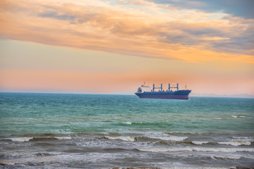 A large ship for cargo entering the port. The sea is a beautiful view of the evening shore. Beautiful sky at sunset.
