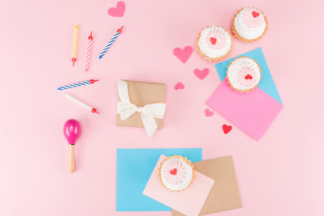 Top view of delicious cupcakes, colorful candles and hearts symbols on pink, birthday party concept