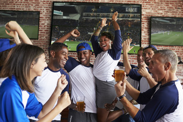 Friends Watching Game In Sports Bar On Screens Celebrating