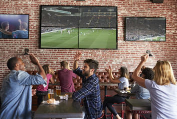 Friends Watching Game In Sports Bar On Screens Celebrating - obrazy, fototapety, plakaty