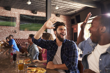 Friends At Counter In Sports Bar Watch Game And Celebrate