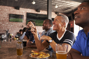 Male Friends At Counter In Sports Bar Watching Game