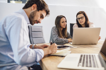 Group of young business people working at start-up in office with laptop and notepad