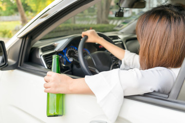 Drunk woman driving and holding beer bottle outside a car.