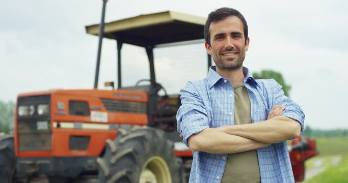 Portrait of a handsome young farmer standing in a shirt and smiling at the camera, on a tractor and nature background. Concept: bio ecology, clean environment, beautiful and healthy people, farmers.
