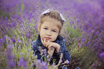 Pretty young girl sitting in lavender field in nice hat boater with purple flower on it.