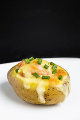 Close up of a hot baked potato topped with sour cream, bacon, green onions and cheddar cheese.