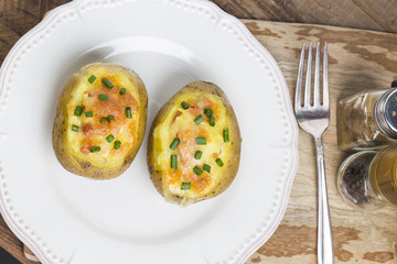Close up of a hot baked potato topped with sour cream, bacon, green onions and cheddar cheese.