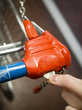 Locking and unlocking the supermarket trolley with one euro coin for grocery shopping,