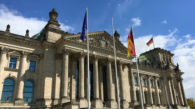 Eingang Deutscher Bundestag Berlin mit wehenden Deutschland-Flaggen bei sch&ouml;nem Wetter mit blauen Himmel und Sonnenschein