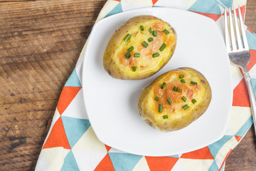 Close up of a hot baked potato topped with sour cream, bacon, green onions and cheddar cheese.