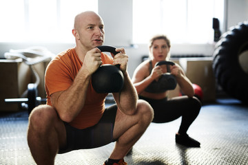 Young sporty woman and middle-aged bodybuilder doing kettlebell squat exercise during intensive...