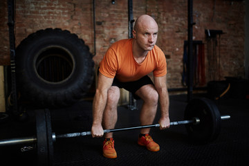 Fototapeta na wymiar Middle-aged fit man working out with barbell in spacious gym, full-length portrait