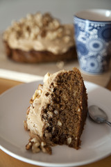 Vertical shot of delicious slice of walnut and coffee cake, with a large cup of coffee in the background
