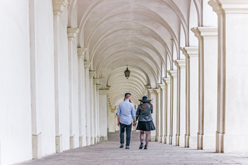 Happy young couple holding hands and walking together under the arches. Young modern hipster couple in love.