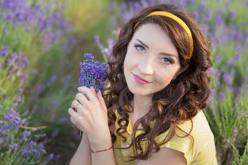 Young mother with young daughter smiling on the field of lavender .Daughter sitting on mother hands.Girl in colorful dress and mother in dark blue dress.