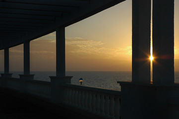Sunset over the ocean framed through a silhouetted building, with large columns and minimalist details
