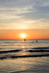 People swim near shadow boat and light sunset on the beach.