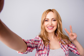 Young beautiful woman in checkered shirt taking self portrait and showing v-sign